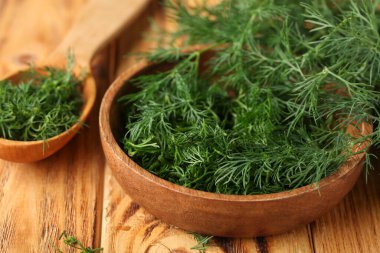 Ahşap arka planda taze yeşil dereotlu kase ve kaşık, yakın plan.