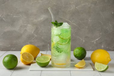 Bir bardak lezzetli soğuk kokteyl ve turunçgil meyveleri beyaz fayans masasında, yakın plan.