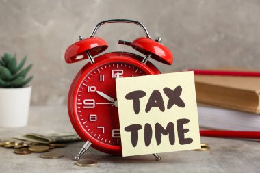 Paralı kitaplar, çalar saat, ev bitkisi ve grunge grisi arkaplan üzerindeki Vergi Zamanı