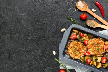 Lezzetli fırında lahana biftekleri, brokoli, patlıcan, taze domates ve grunge siyah arka planda kaşıklar dolusu baharat.