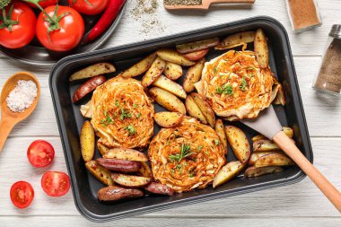 Lezzetli fırında lahana biftekleri, patatesler, taze domatesler ve beyaz ahşap arka planda baharatlar.