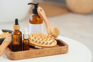 Farklı masaj fırçaları, deniz tuzu ve kozmetik ürünleri olan tepsi banyodaki masada.