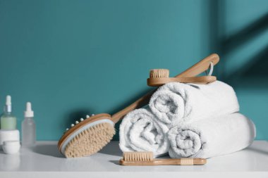 Katlanmış havlular ve kozmetik ürünlerle farklı masaj fırçaları banyoda mavi duvarın yanında klozette.