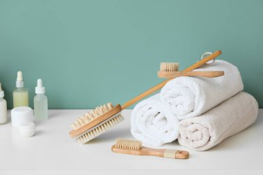 Katlanmış havlular ve kozmetik ürünlerle farklı masaj fırçaları banyoda mavi duvarın yanında klozette.