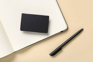 Bej arka planda not defteri ve kalemle boş bir siyah kartvizit.