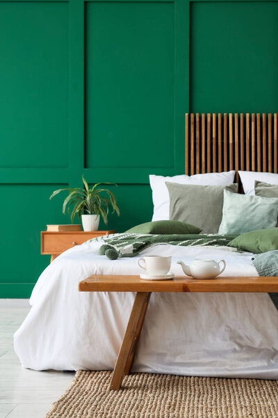 Интерьер стильной спальни с уютной кроватью и деревянной скамейкой у кровати