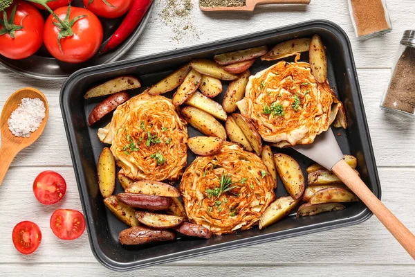 Lezzetli fırında lahana biftekleri, patatesler, taze domatesler ve beyaz ahşap arka planda baharatlar.