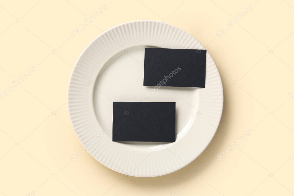 Plate with blank black business cards on beige background
