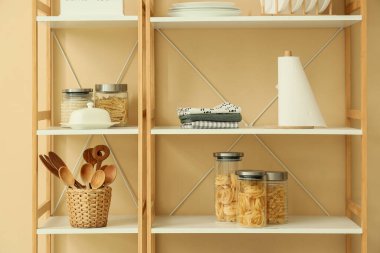 Mutfak aletleri ve bej duvarın yanında yiyecek olan raf ünitesi.