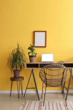 Ofiste sarı duvarın yanında dizüstü bilgisayarı ve bitkileri olan modern bir iş yeri.