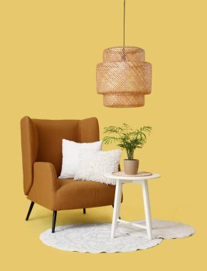 Yastıklı rahat bir koltuk ve sarı arka planda bitkileri olan kahve masası.