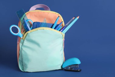 Mavi arka planda okul malzemeleri olan sırt çantası.