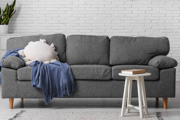 Cozy sofa with pillow and plaid near coffee table with book in interior of living room