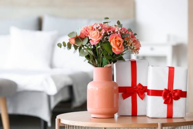 Çiçekli vazo ve Uluslararası Kadınlar Günü için hediye kutuları yatak odasındaki masada, yakın plan.