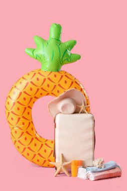 Bavul, plaj aksesuarları, şişirilebilir yüzük ve pembe arka planda dekor.