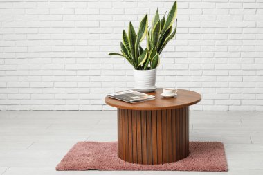 Bitkili ahşap sehpa, bir fincan çay ve beyaz tuğla duvarın yanında dergi.