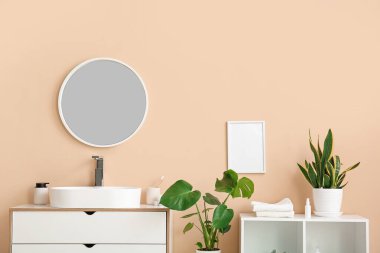 Seramik lavabo, ayna ve çekmeceler banyoda bej duvarın yanında.