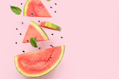 Uçan taze karpuz parçaları ve pembe arka planda nane ve tohumlar.