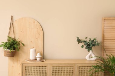 Ahşap çekmeceler, ev bitkisi ve oturma odasındaki bej duvarın yanında katlanır ekran.