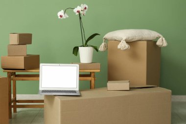 Boş dizüstü bilgisayar, taşınan kutular ve yeşil duvarın yanında orkide çiçeği.