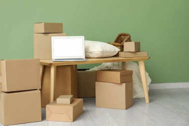 Masada yastık ve yeşil duvarın yanındaki kutuları taşıyan boş bir laptop.