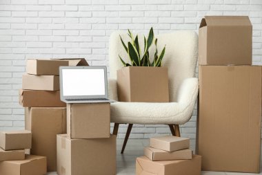 Boş dizüstü bilgisayar, taşınan kutular ve beyaz tuğla duvarın yanındaki koltuk.