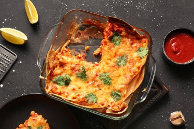 Lezzetli enchilada ve domates soslu koyu arkaplanda cam pişirme tabağı.