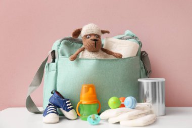 Bebek çantasında pembe arka planda koyun oyuncağı var.