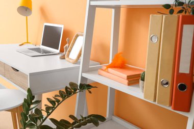 Turuncu duvarın yanında modern dizüstü bilgisayarı olan rahat bir çalışma alanı