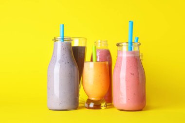 Sarı arka planda farklı taze meyve suyu kadehleri ve şişeleri.