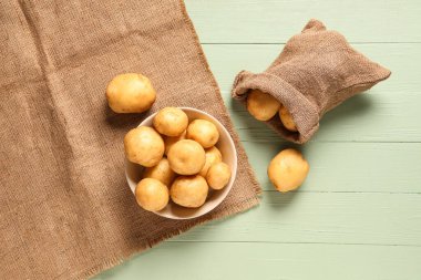 Yeşil ahşap arka planda çiğ patates dolu kase ve çuval.