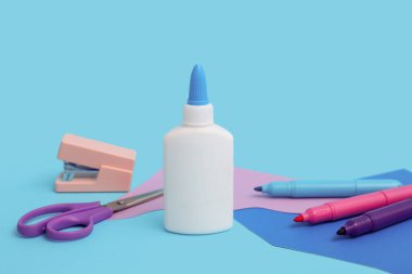 Bir şişe tutkal, keçeli kalem ve makas mavi arka planda.