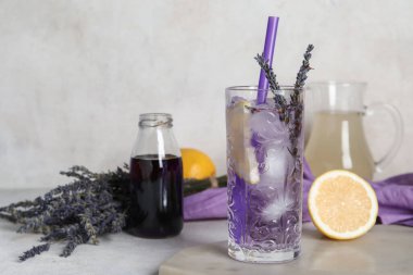 Bir bardak soğuk lavantalı limonata, çiçekler ve açık arkaplanda şurup.