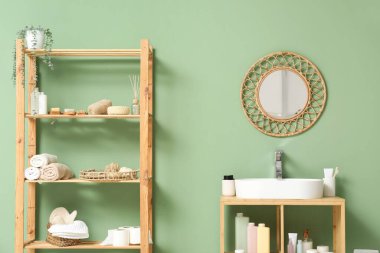 Lavabosu, aynası ve banyo aksesuarları olan raf ünitesi yeşil duvarın yanında.