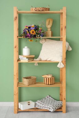 Yeşil duvarın yanında yabani çiçekli raf ünitesi.