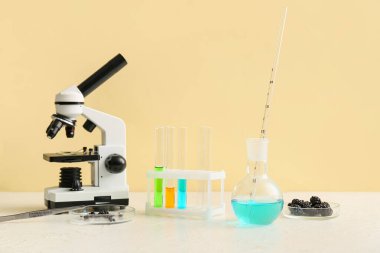 Mikroskop ve böğürtlenli profesyonel laboratuvar bardakları sarı duvarın yanındaki masada.