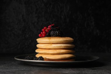 Taze böğürtlenli krep tabağı ve siyah arka planda kırmızı frenk üzümü.
