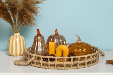 Süslü balkabağı tepsisi, köknar kozalakları ve mavi duvarın yanındaki rafta yanan mum.