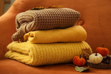 Turuncu koltukta sonbahar süslemeleri olan şık kıyafetler yığını oturma odasında, yakın plan.