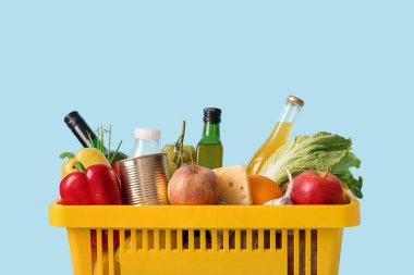 Farklı taze ürünler ve elmalarla dolu sarı alışveriş sepeti mavi arka planda