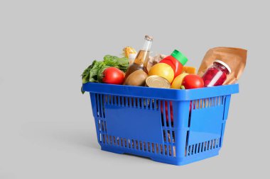 Beyaz arka planda farklı taze ürünler ve domateslerle dolu mavi alışveriş sepeti.