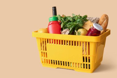 Farklı taze ürünlerle dolu sarı alışveriş sepeti ve bej arka planda ketçap.