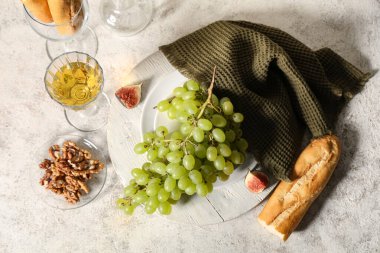 Beyaz zemin üzerinde tatlı üzümler, cevizler, baget ve bir bardak şarap.
