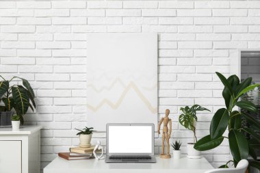 Ofiste beyaz tuğla duvarın yanında boş dizüstü bilgisayarı ve yeşil bitkileri olan işyeri