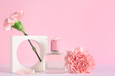 Bir şişe parfüm, alçı standı ve pembe arka planda karanfil çiçekleri.