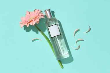 Bir şişe parfüm, Gerbera çiçeği ve turkuaz arka planda taç yaprakları.