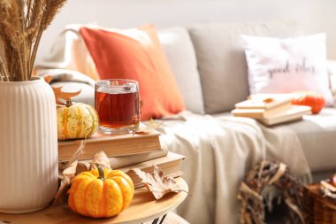 Oturma odasındaki masada balkabaklı, kitaplı ve sonbahar yapraklı bir bardak sıcak çay.
