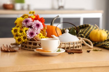 Hasır tabla, çaydanlık, bir fincan sıcak yeşil çay, çiçekler ve sonbahar yaprakları mutfakta.