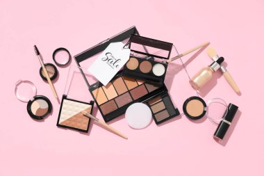 Dekoratif kozmetik ürünleri, makyaj fırçaları ve pembe arka planda satış etiketi olan kompozisyon