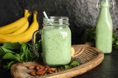 Bardak ve bir şişe taze ıspanaklı smoothie badem fıstığı, chia tohumu ve siyah arka planda muz.